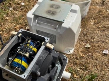 Disassembled electrical device with visible coils and wires on grass.