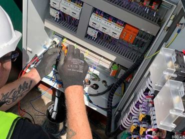 Electrician working on wiring inside a control panel.