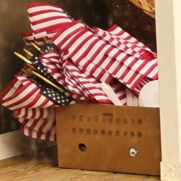 Box filled with multiple American flags on wooden floor.