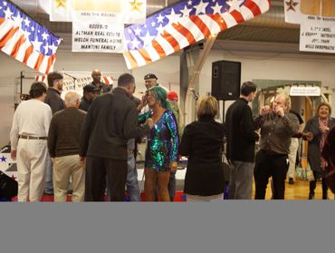 People gather and chat at an indoor event with patriotic decorations.