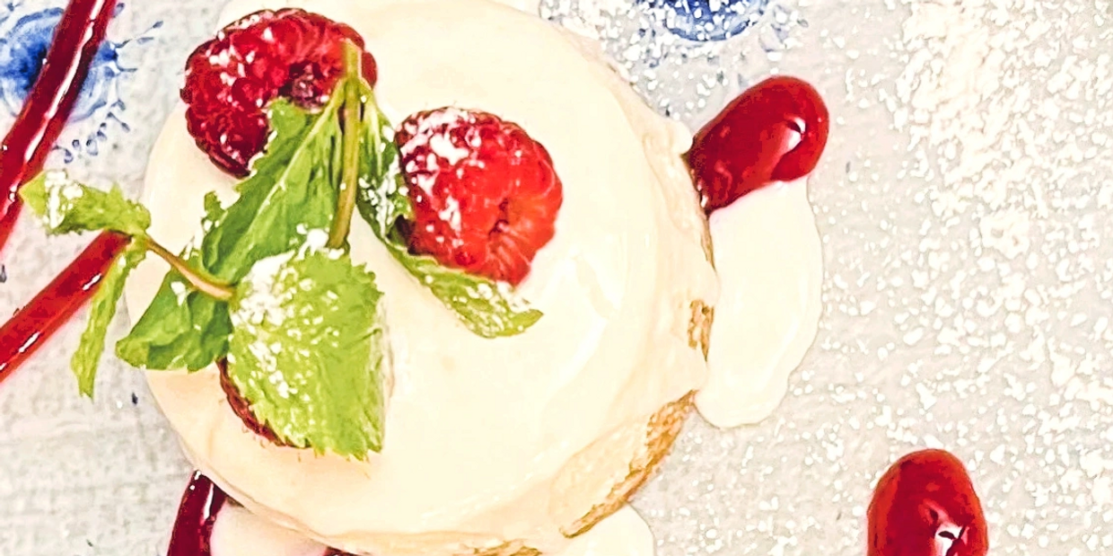 Cream, raspberries, mint, and berry sauce on a decorated plate, the perfect Italian dessert.