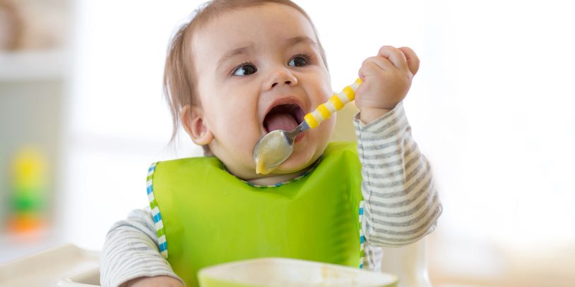 happy baby child sitting in chair with a spoon
