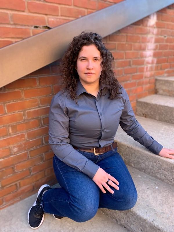 Person with curly hair kneeling on steps against a brick wall.
