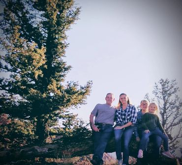 family photo of parents and two children sitting on a fallen tree taken at homeschool camp and learn