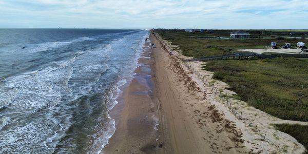 A long sandy beach with waves and a few vehicles parked along the shore.