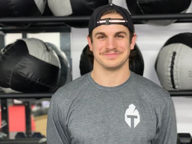 Young man in a gray shirt and backward cap smiling in a gym.