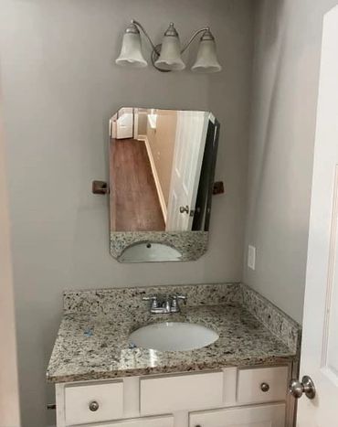 Bathroom vanity with granite countertop and a small mirror above.