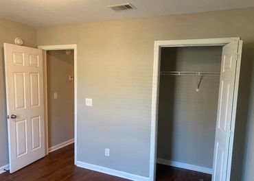 Empty room with beige walls, wooden floor, and open doors.