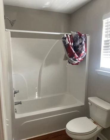 Simple bathroom with bathtub, shower, toilet, and folded floral shower curtain.