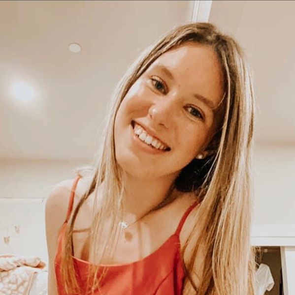 Smiling woman with long blonde hair wearing a red top indoors.