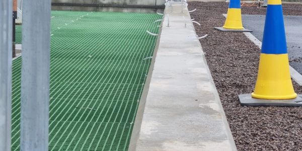 Green grid flooring next to concrete curb and yellow-blue cones.