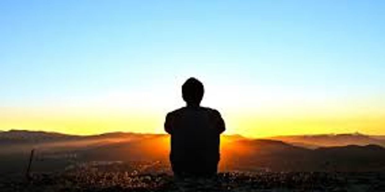 Silhouetted man sitting before a sunset