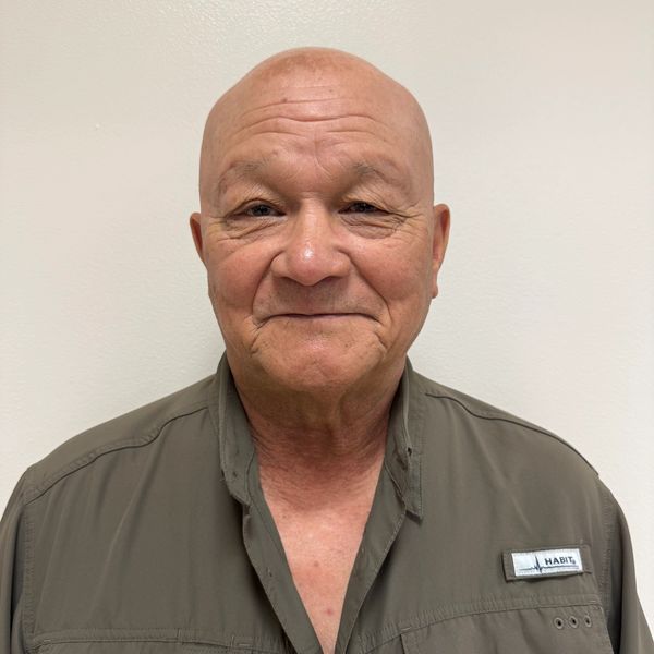 Portrait of a smiling elderly man in a brown shirt against a plain background.