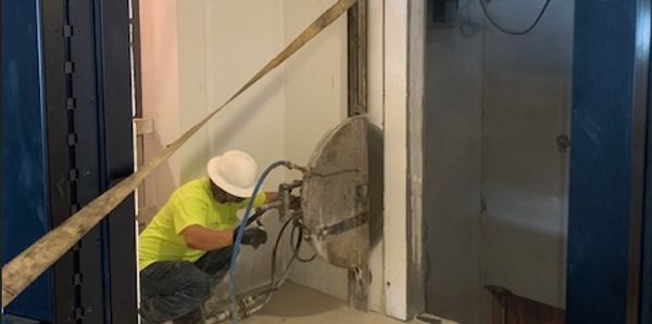 Worker in safety gear operating a wall-cutting machine indoors.