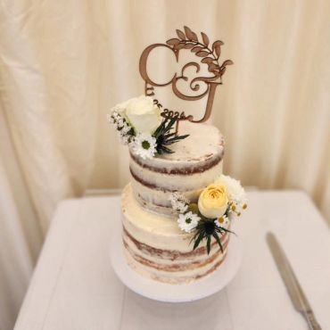 Two-tiered naked cake decorated with flowers and a wooden topper.