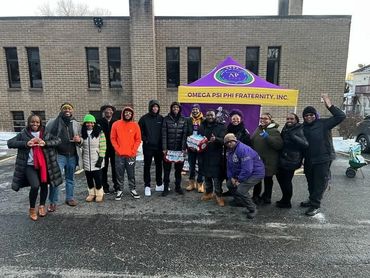 Group of people posing outdoors with Omega Psi Phi Fraternity banner.