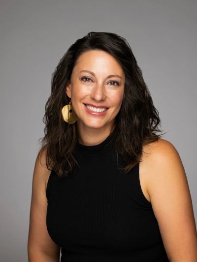 Smiling woman with dark hair and large gold earrings in black sleeveless top.