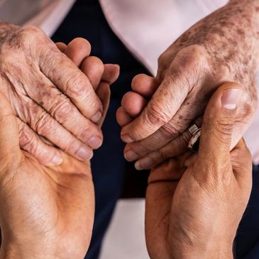 Younger hands gently holding older hands in a caring gesture.