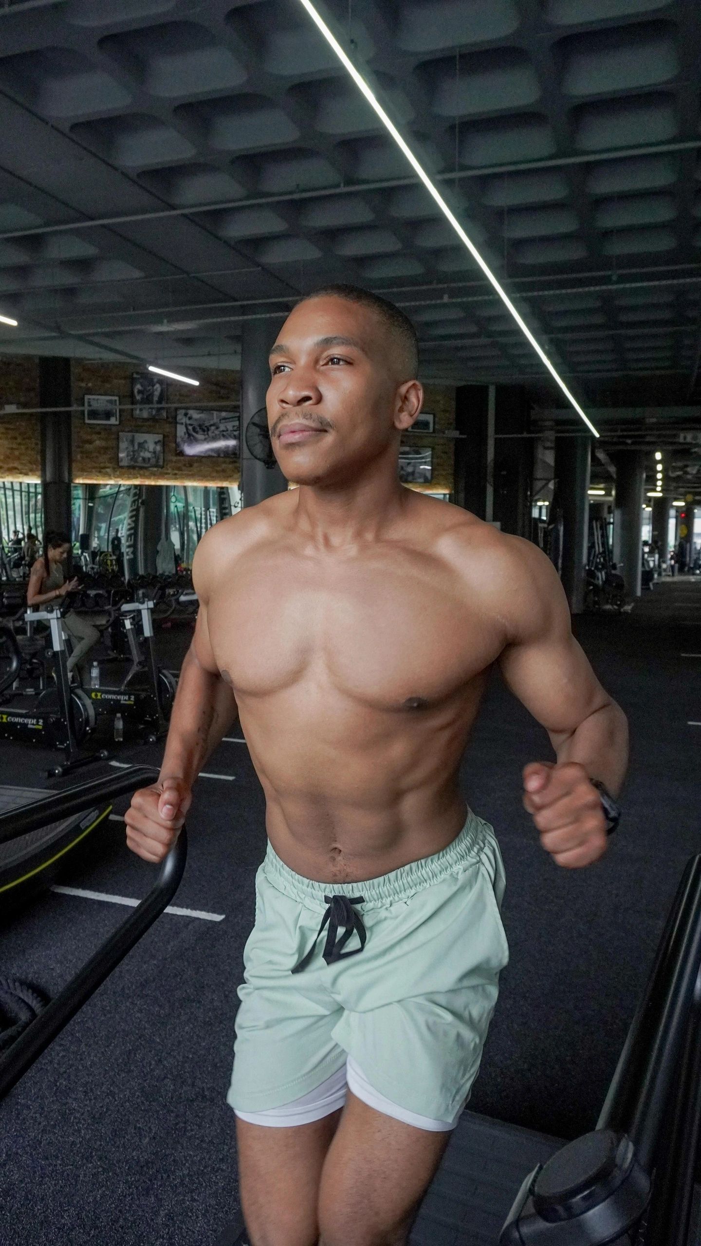 Shirtless man running on a treadmill in a gym.