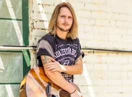 Handsome young man holding the guitar he uses to provide Live Therapeutic Music to hospital patients