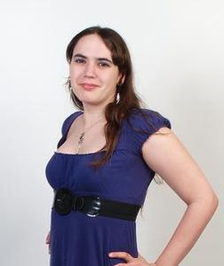 A young woman in a dress smiling at the camera with her hands on her hips.