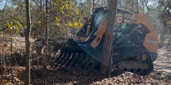 Skid Steer with grappler hook attachment cleaning up general forest debris.