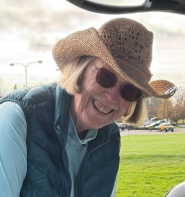 Smiling woman in sunglasses and a woven cowboy hat outdoors.