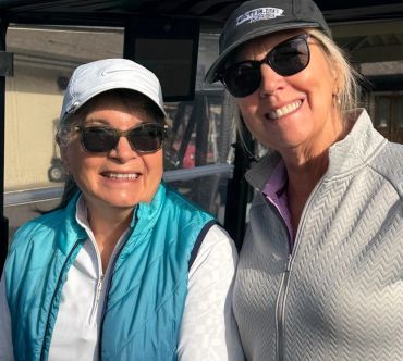 Two women smiling outdoors wearing sunglasses and hats.