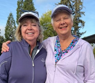Two smiling women outdoors wearing golf attire and caps.