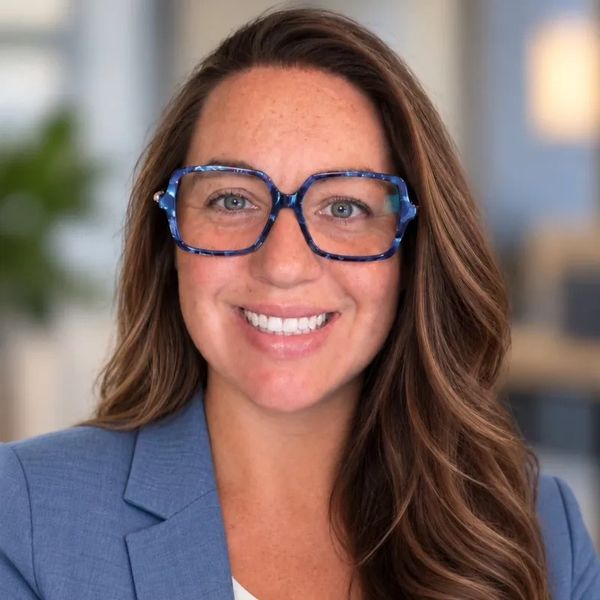 Smiling woman in glasses and blue blazer.