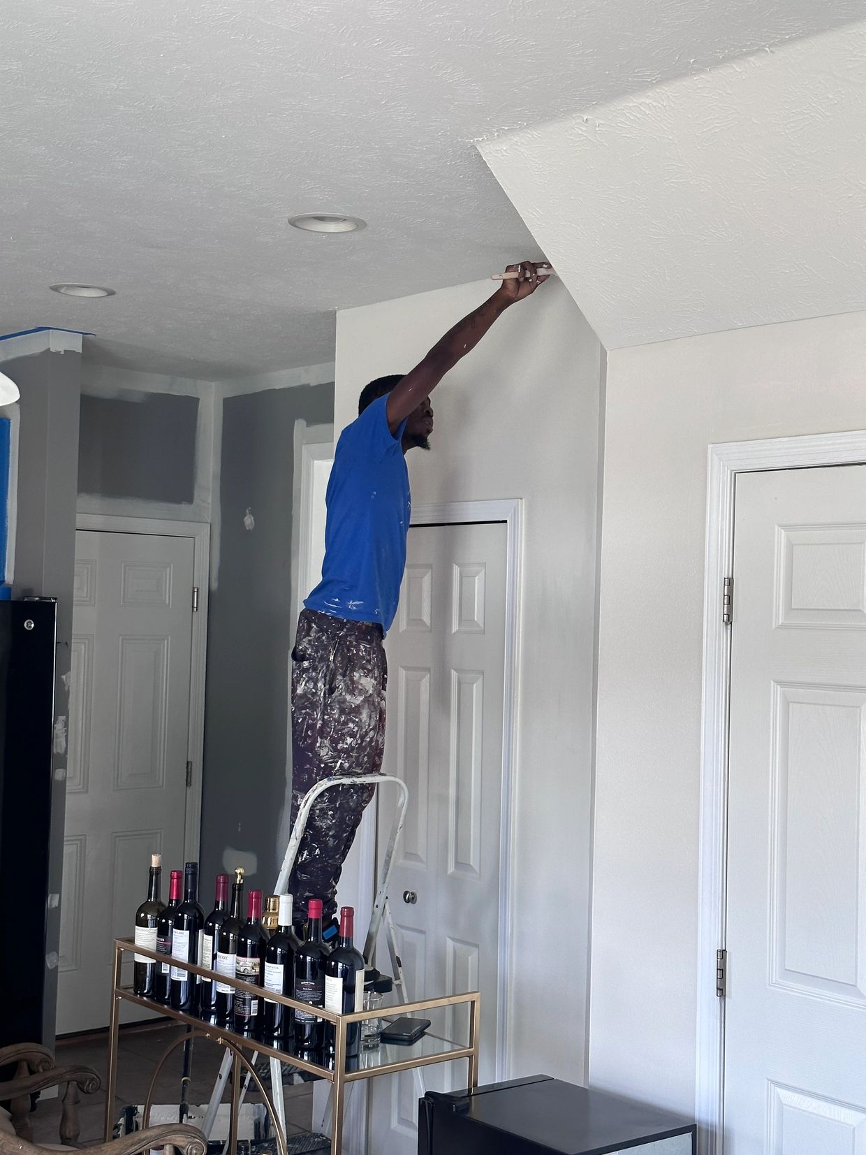 Man painting ceiling edge while standing on a ladder.