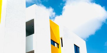 Edificio moderno blanco con detalles amarillos bajo un cielo azul.
