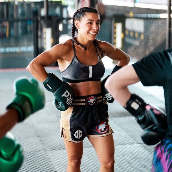 A female boxer smiling during training, wearing gloves and sportswear.