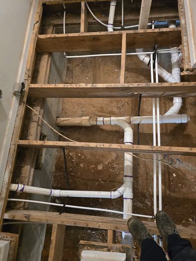 Exposed floor joists with visible plumbing pipes and wiring during construction or renovation.