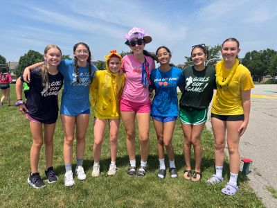Group of smiling girls in colorful outfits outdoors on a sunny day.