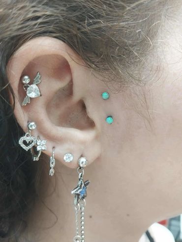 Ear adorned with multiple silver and turquoise piercings including hearts, stars, and gems.