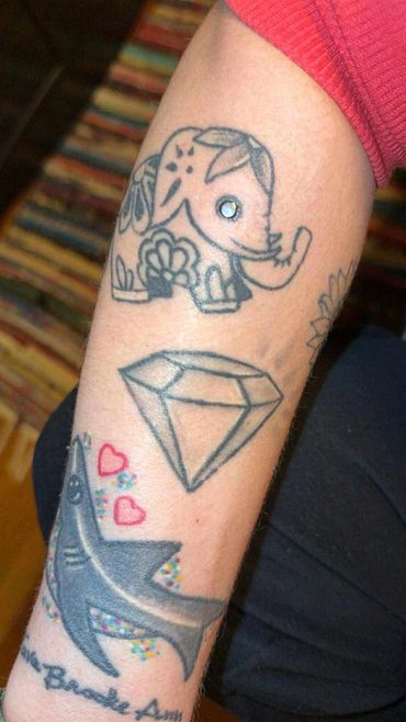 Colorful tattoos of an elephant, diamond, and shark on a forearm.