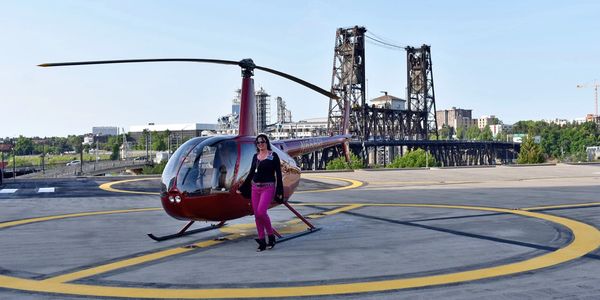 Woman walking away from a red helicopter on a helipad near a bridge.