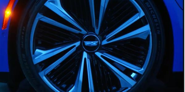 Close-up of a stylish car wheel with a Cadillac logo in blue lighting.