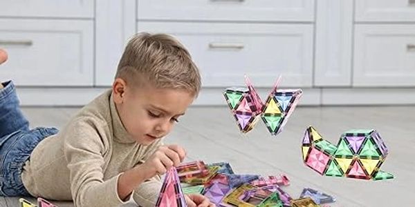 Young boy playing with colorful magnetic building tiles on the floor.