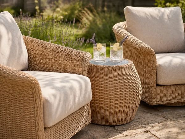 Two wicker armchairs with cushions and a matching wicker side table with drinks.
