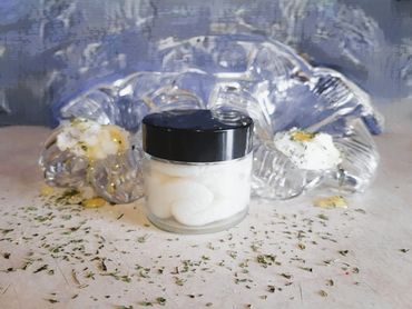 A jar of cream with decorative elements and herbs on a textured surface.