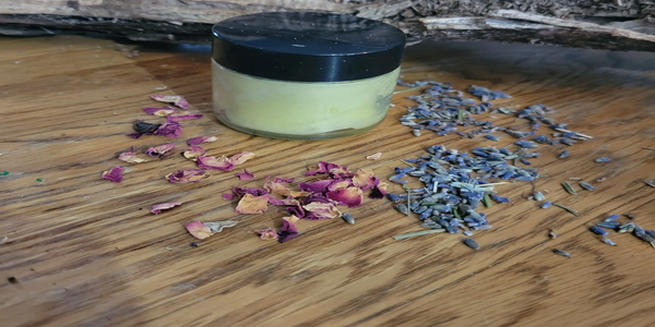 A jar of cream surrounded by dried rose and lavender petals on a wooden surface.