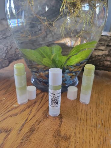Three tubes of mint chapstick on a wooden table with a fishbowl in the background.