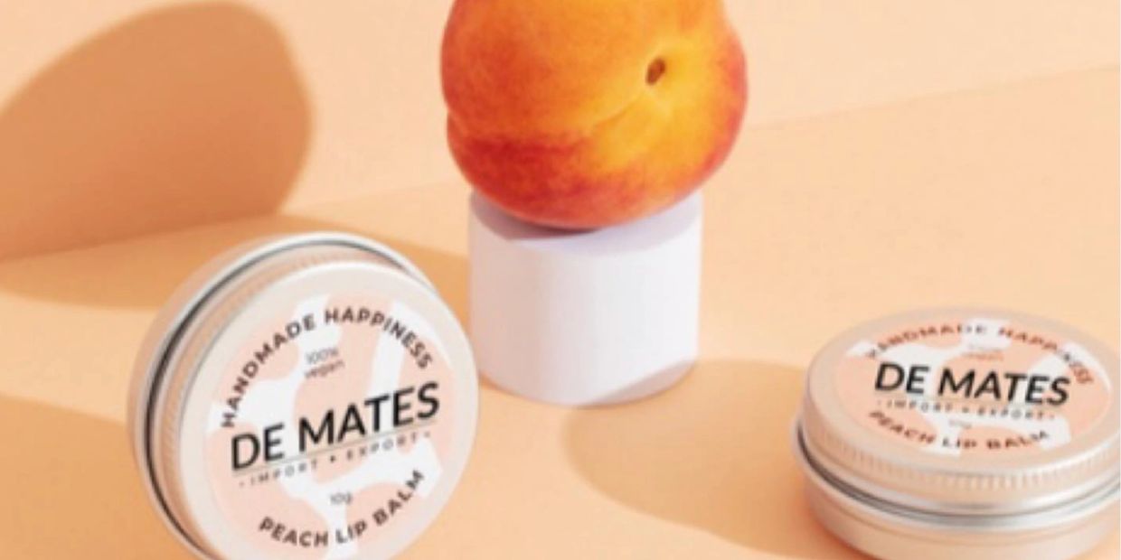 Peach lip balm tins with a fresh peach on a pastel background.