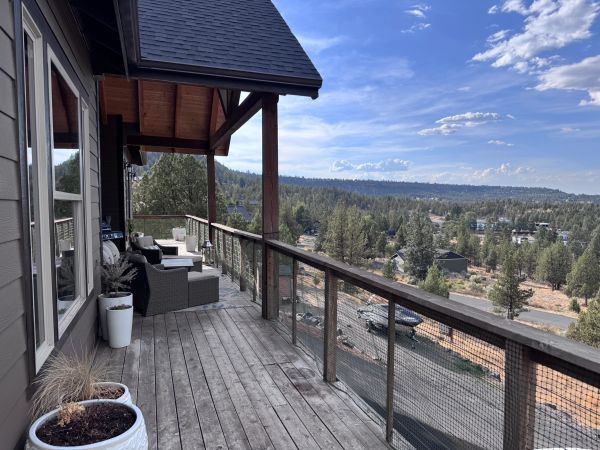 Wooden balcony overlooking a forested landscape under a blue sky.