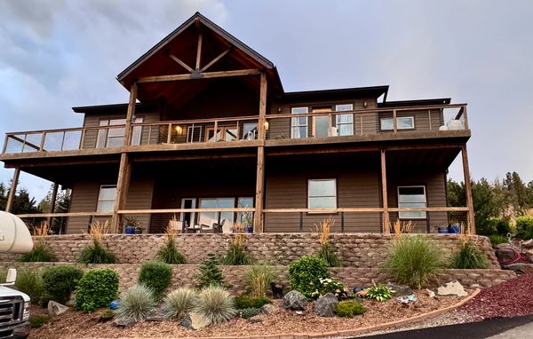 A two-story wooden house with a spacious balcony and landscaped garden.