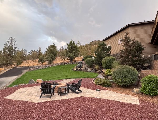 Outdoor patio with black chairs and a fire pit surrounded by landscaped greenery.
