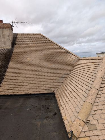 Roof with beige tiles and a chimney under a cloudy sky.