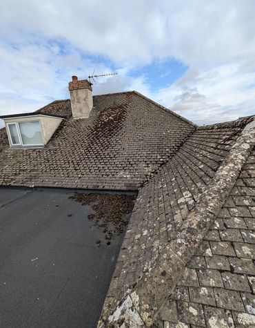 Old roof with moss and weathered tiles under a cloudy sky.